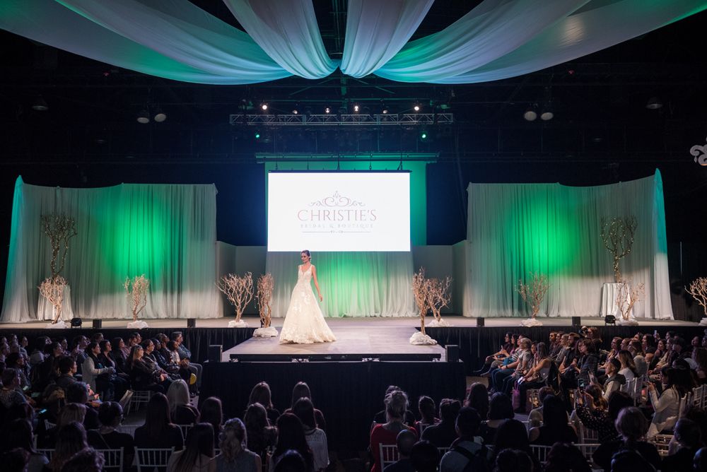 A woman in a wedding dress is walking down a runway at a wedding show.