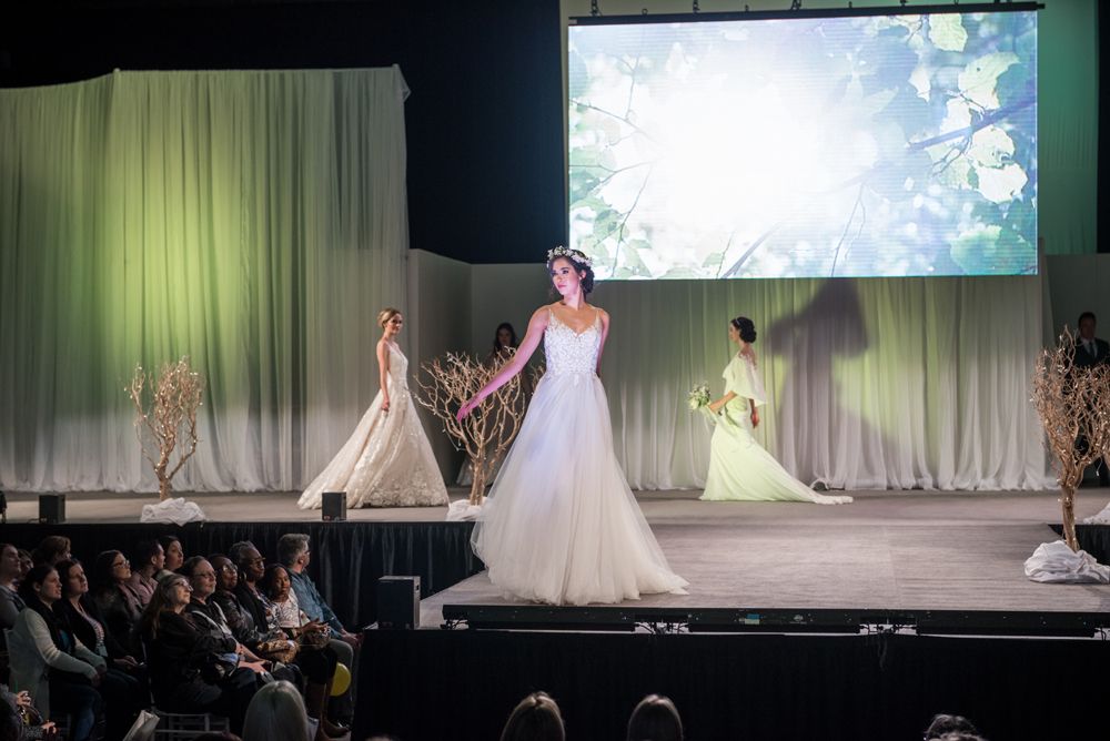 A group of women in wedding dresses are walking down a runway at a wedding show.