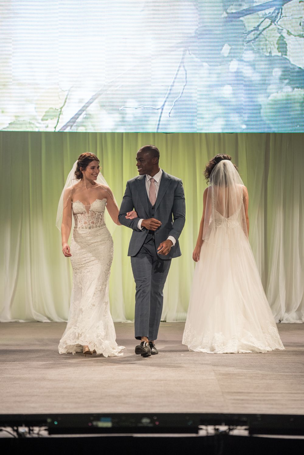 A bride and groom are walking down the runway at a wedding show.