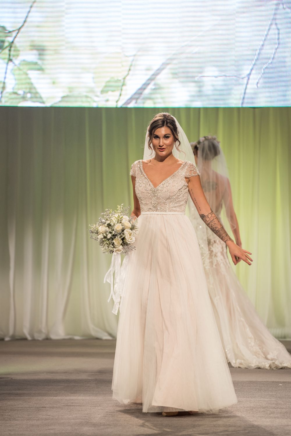 A woman in a wedding dress is walking down a runway holding a bouquet of flowers.