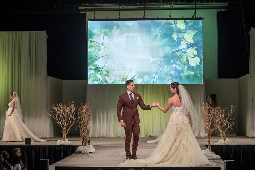 A bride and groom are walking down a runway at a wedding show.