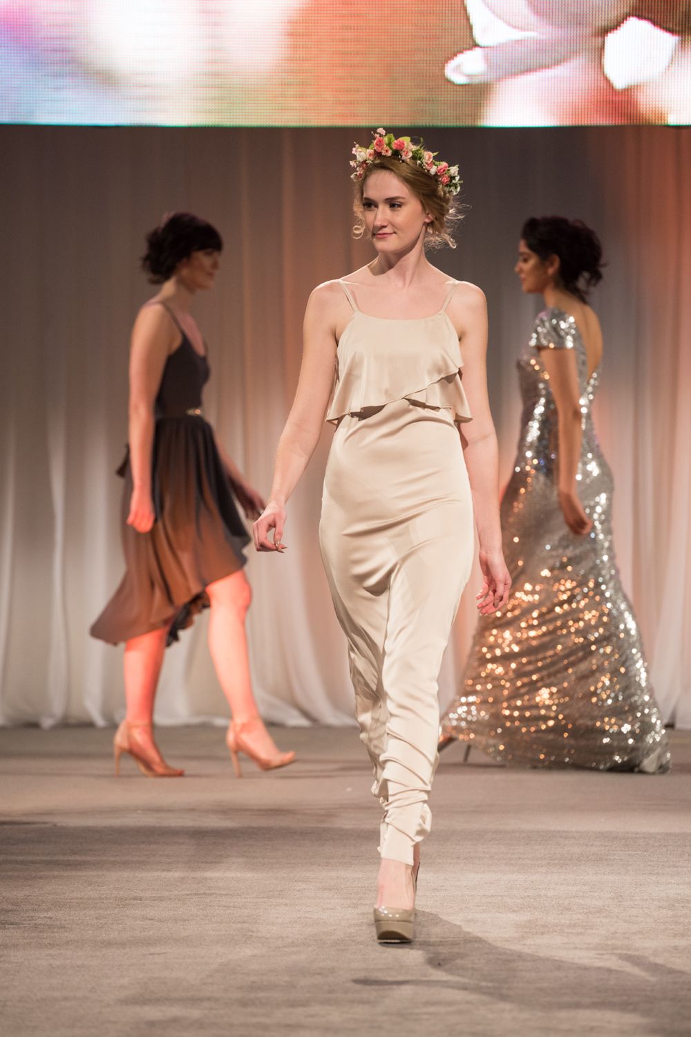 A woman in a white dress is walking down a runway at a fashion show.