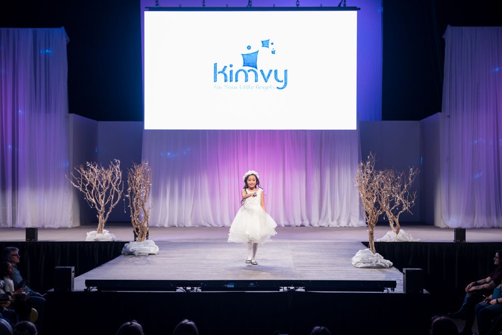A little girl is walking down a runway at a fashion show.