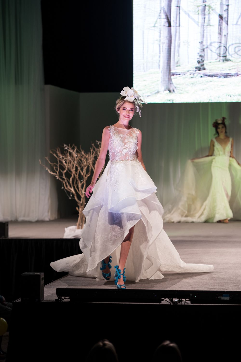 A woman in a wedding dress is walking down a runway at a fashion show.