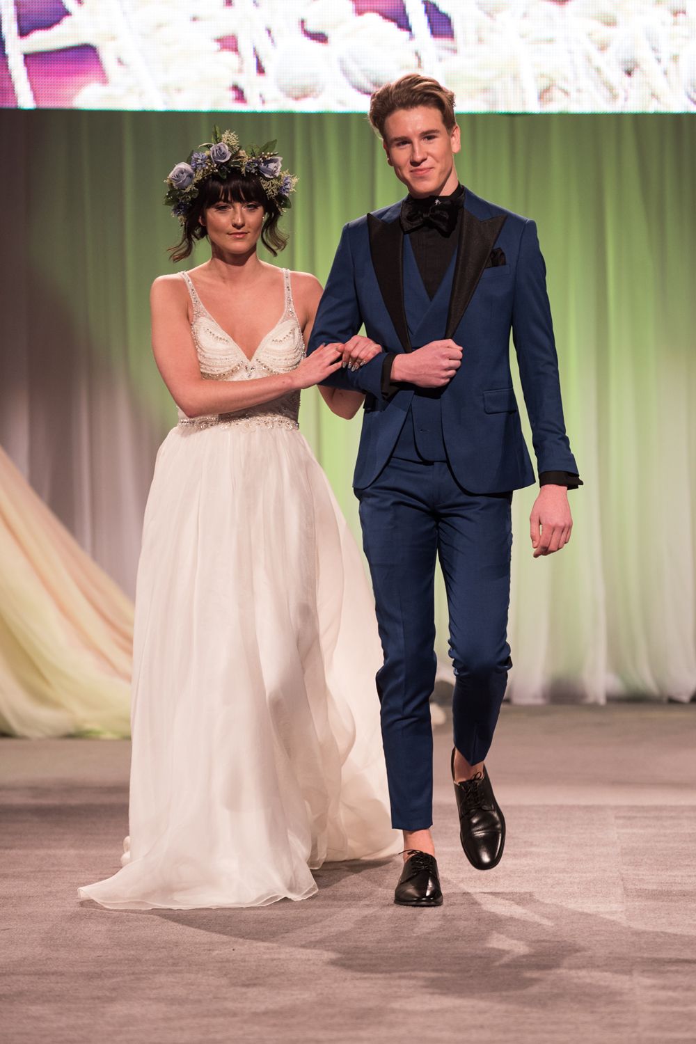 A bride and groom are walking down a runway at a wedding show.