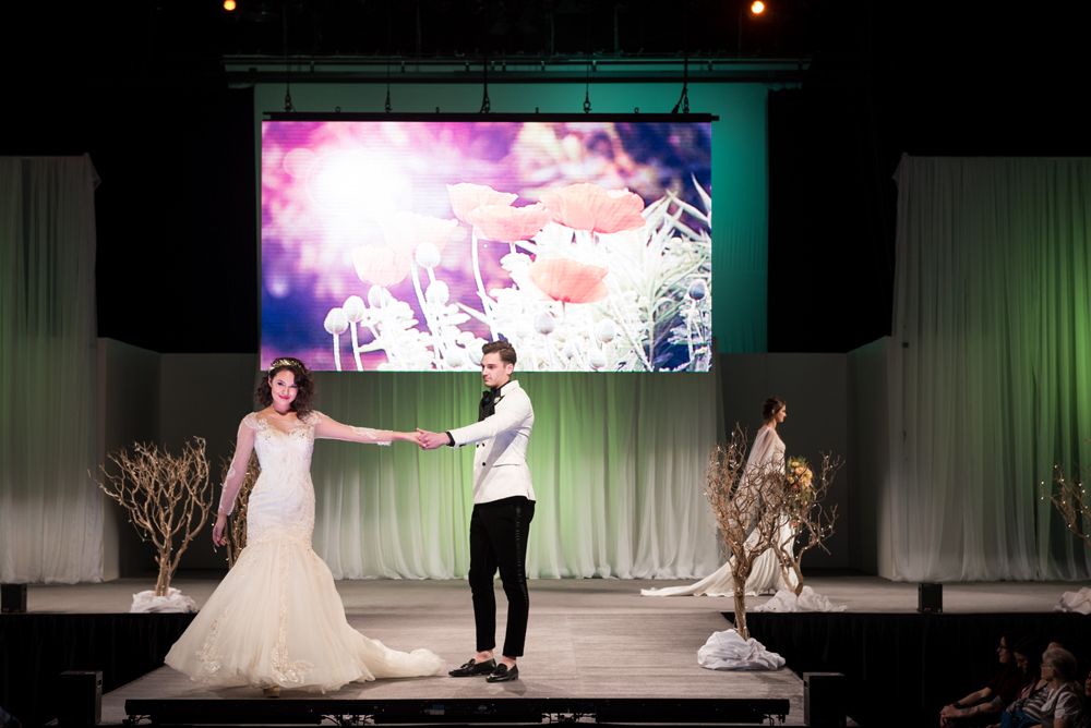 A bride and groom are dancing on a stage in front of a large screen.