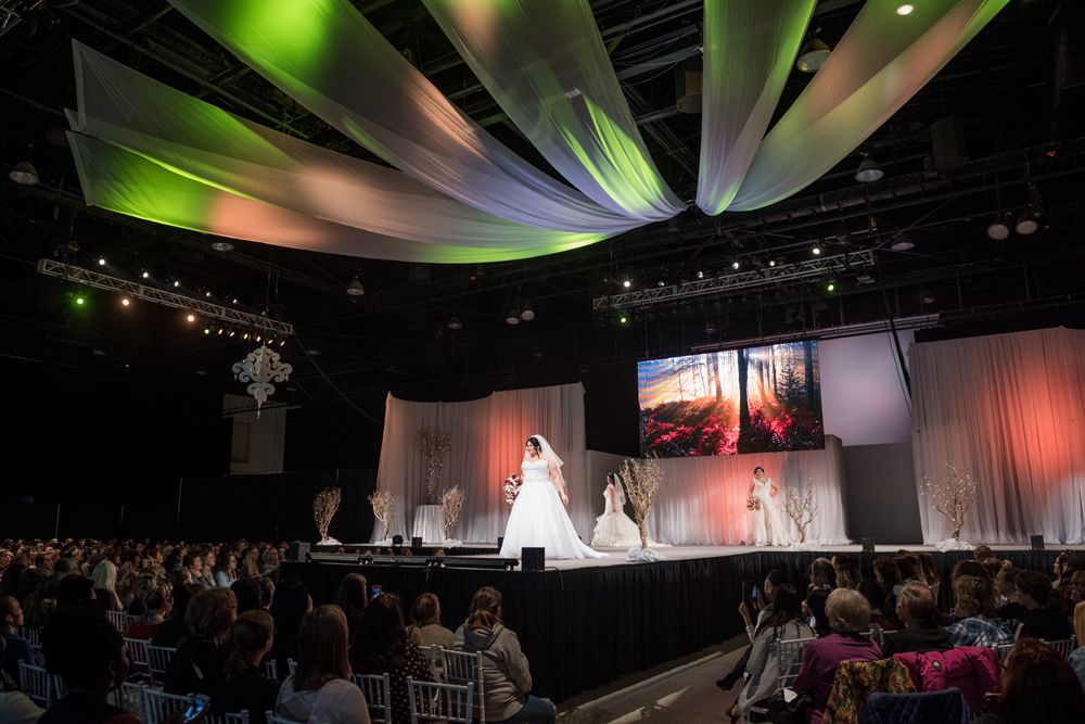A woman in a wedding dress is walking down a runway at a wedding show.
