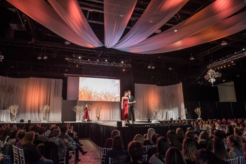 A group of people are sitting in a large room watching a fashion show.