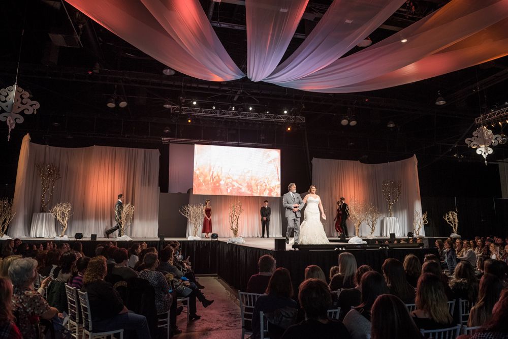 A bride and groom are walking down a runway at a wedding show.