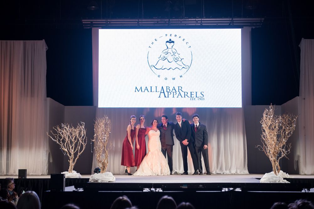 A group of people are standing on a stage in front of a large screen.
