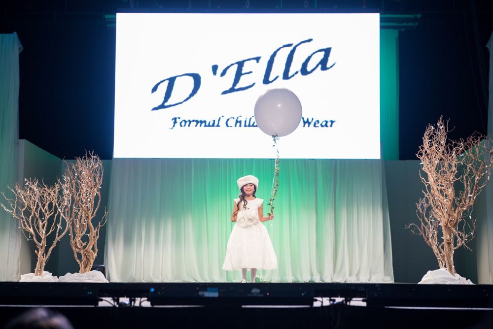 A little girl is holding a balloon on a stage in front of a d ' ella logo