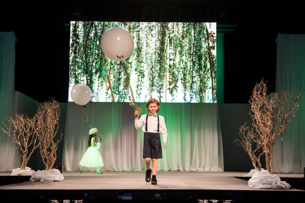 A young boy is walking down a runway at a fashion show.