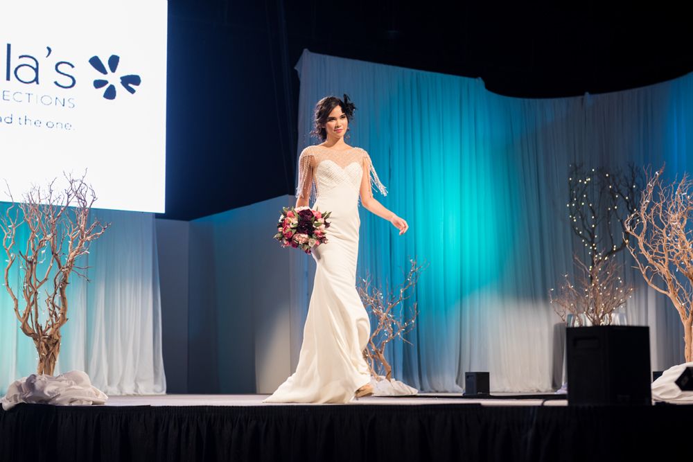 A woman in a wedding dress is walking down a runway at a wedding show.