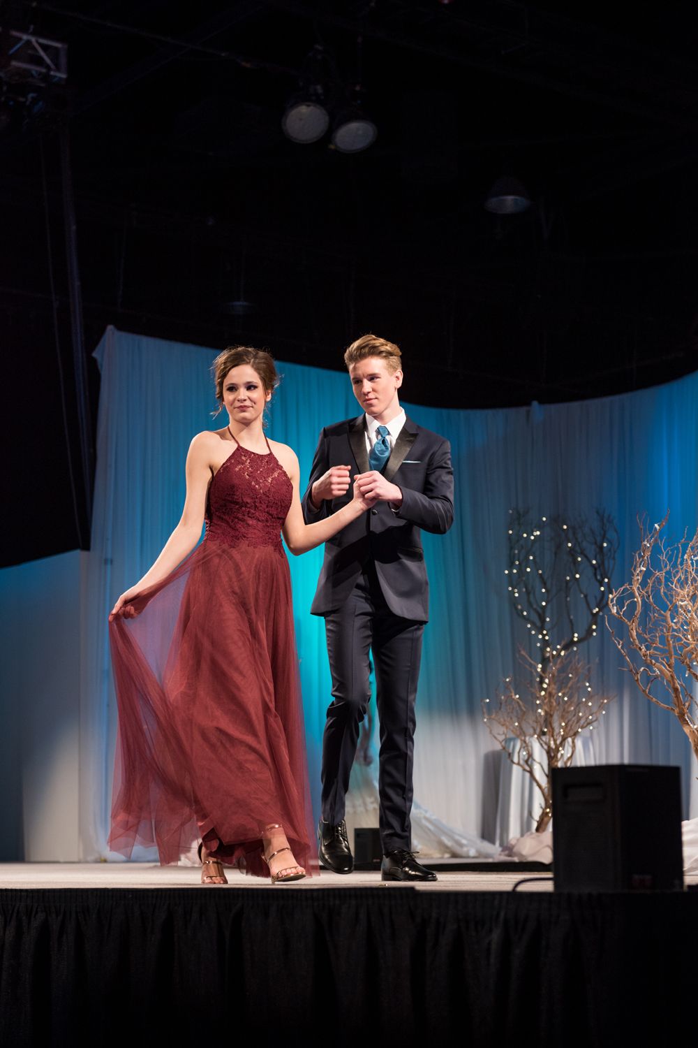 A man and a woman are walking on a stage holding hands.