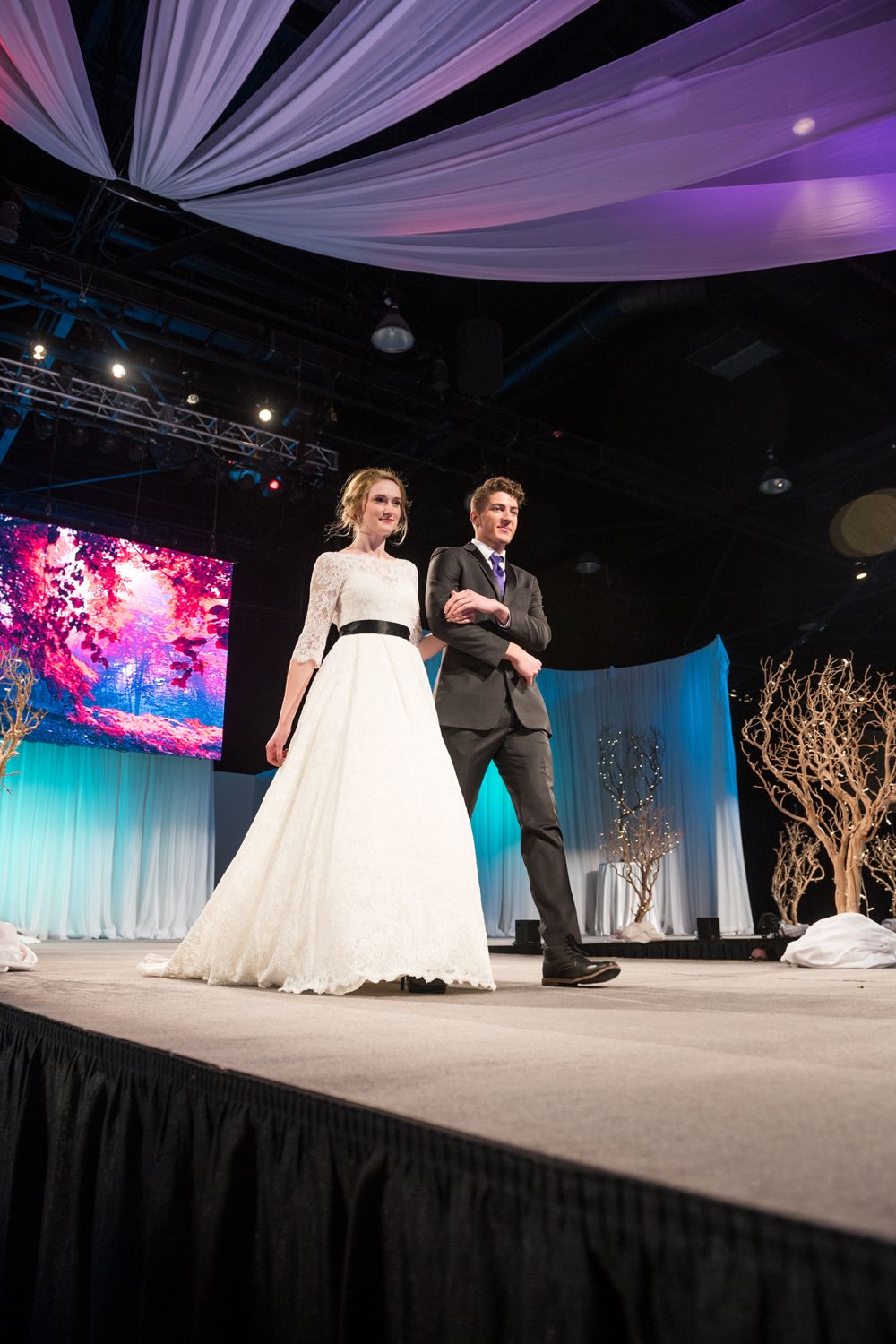 A bride and groom are walking down a runway at a wedding show.
