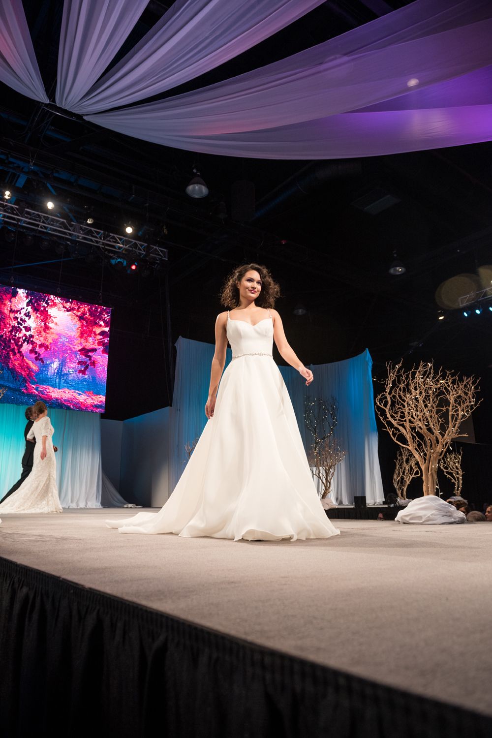 A woman in a wedding dress is walking down a runway at a wedding show.