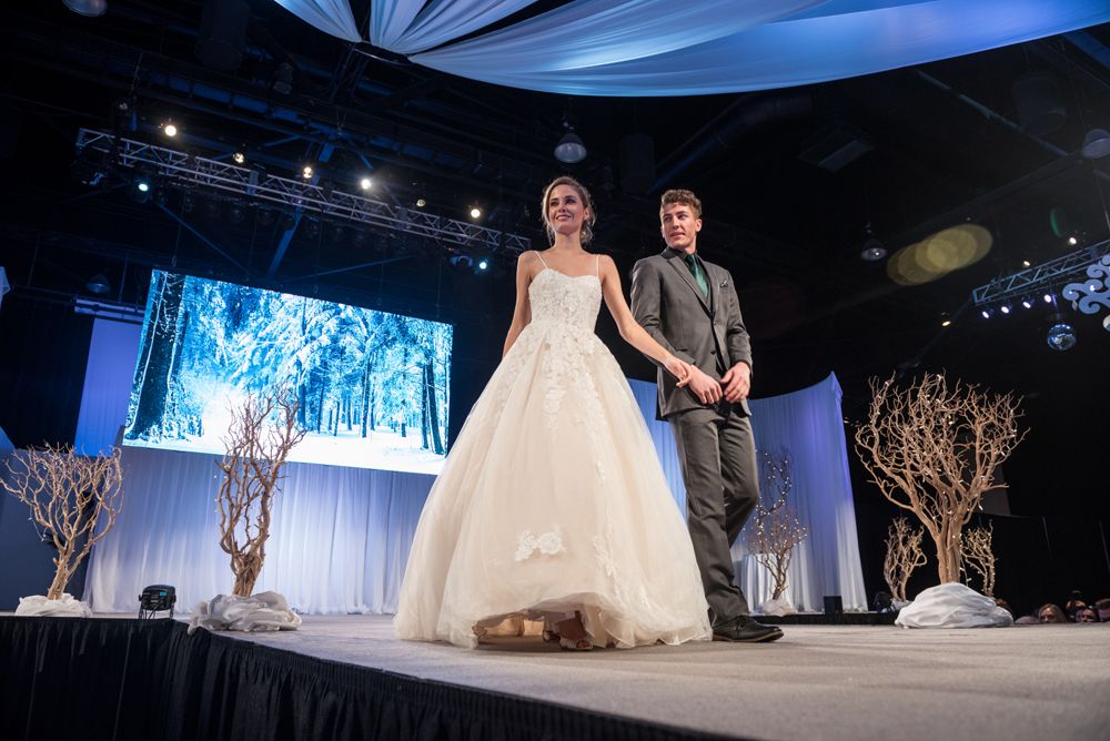 A bride and groom are walking down a runway at a wedding show.