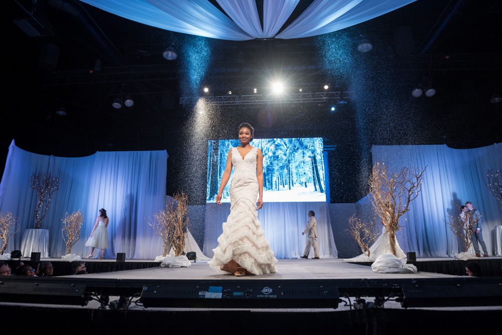 A woman in a wedding dress is walking down a runway at a fashion show.