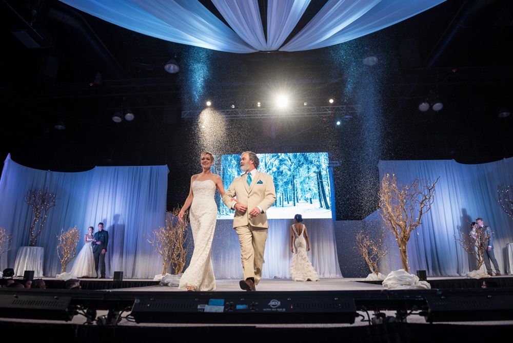 A bride and groom are walking down a runway at a wedding show.