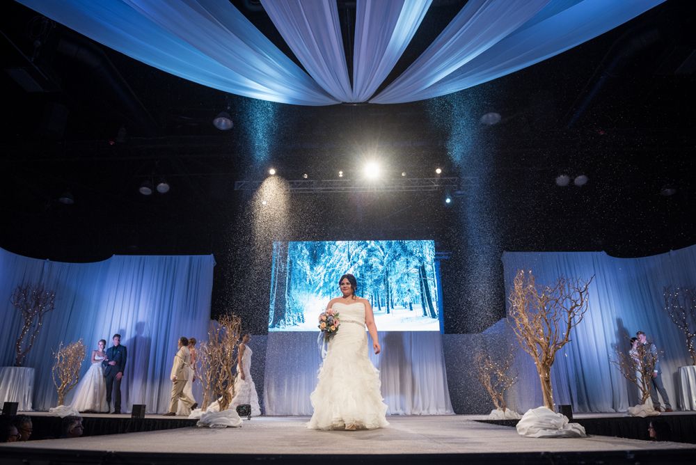 A bride is walking down a runway at a wedding show.