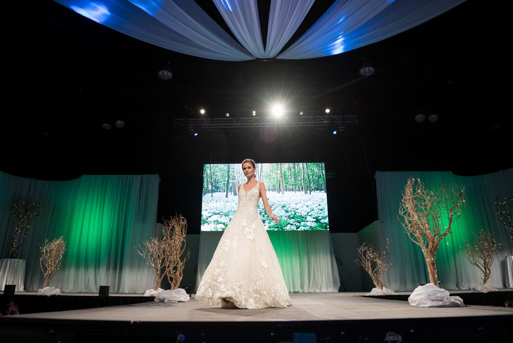 A woman in a wedding dress is walking down a runway at a wedding show.