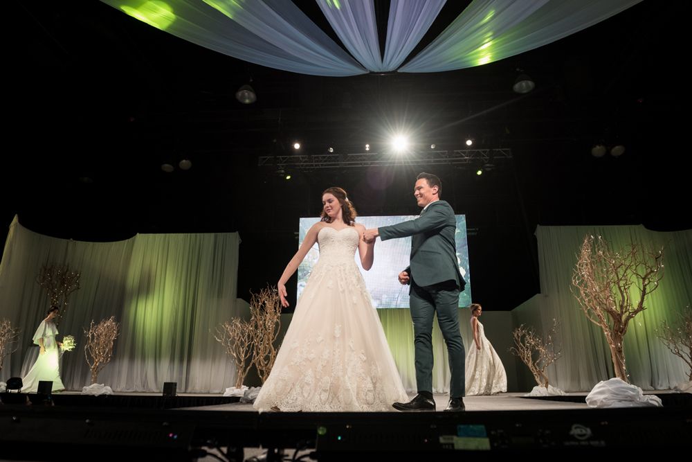 A bride and groom are dancing on a stage at a wedding show.