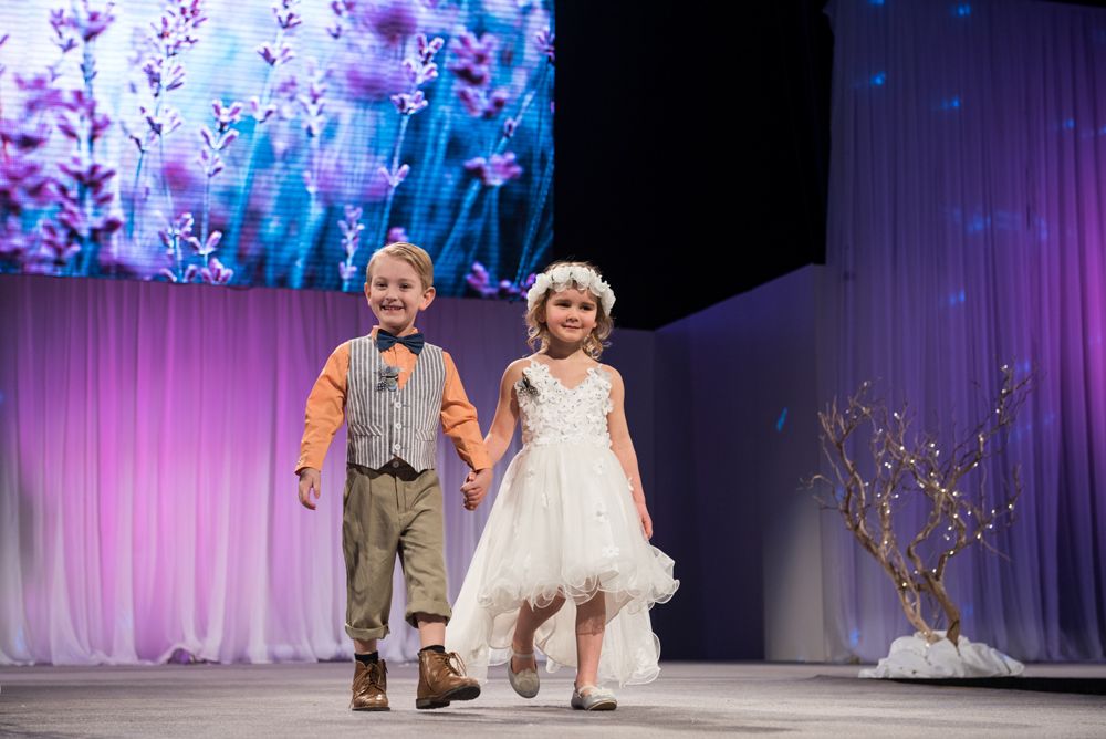A boy and a girl are walking down a runway at a fashion show.
