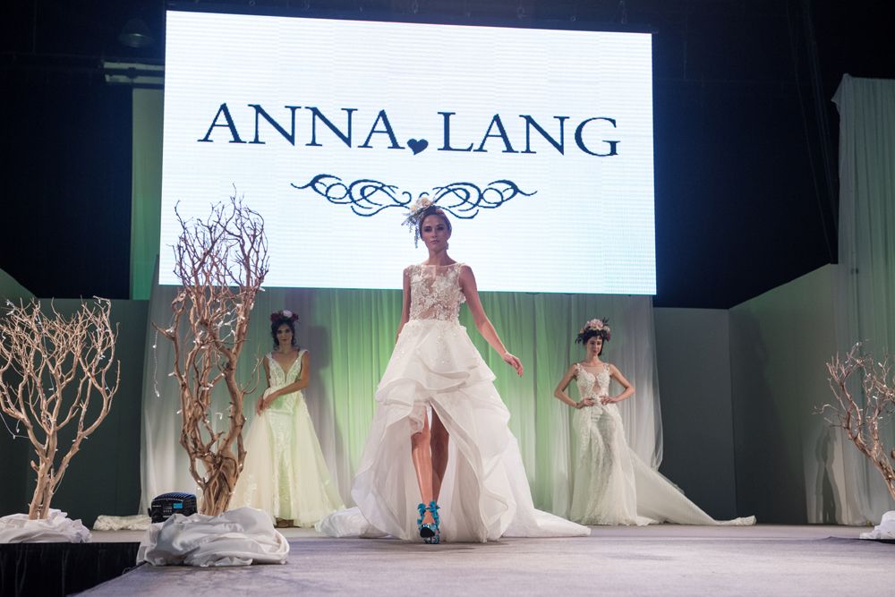 A woman in a wedding dress is walking down a runway at a fashion show.