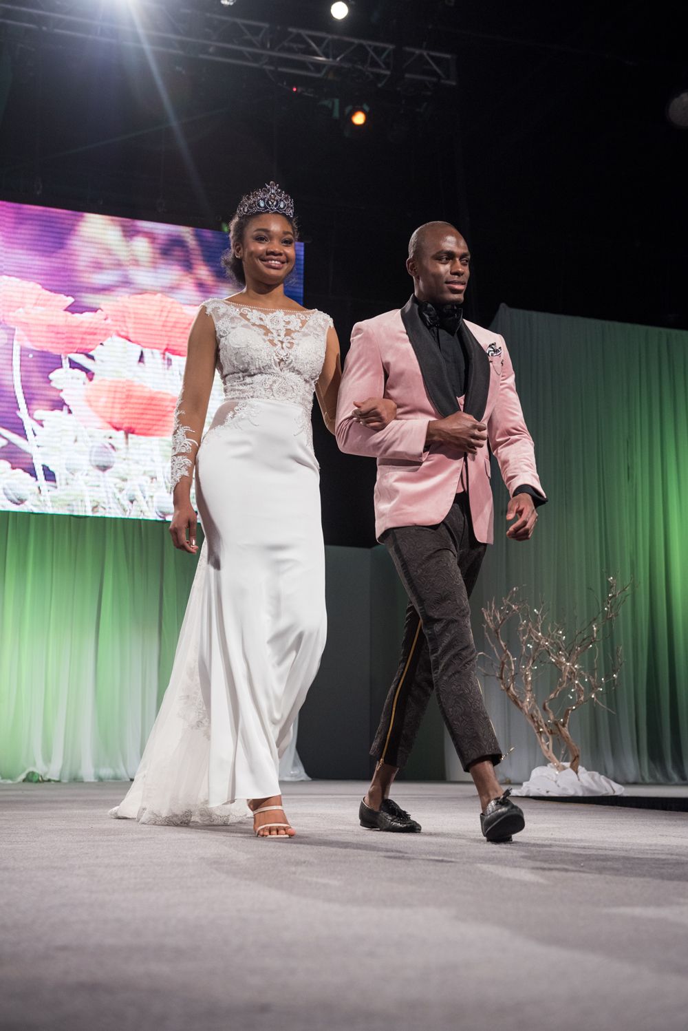 A bride and groom are walking down a runway at a fashion show.
