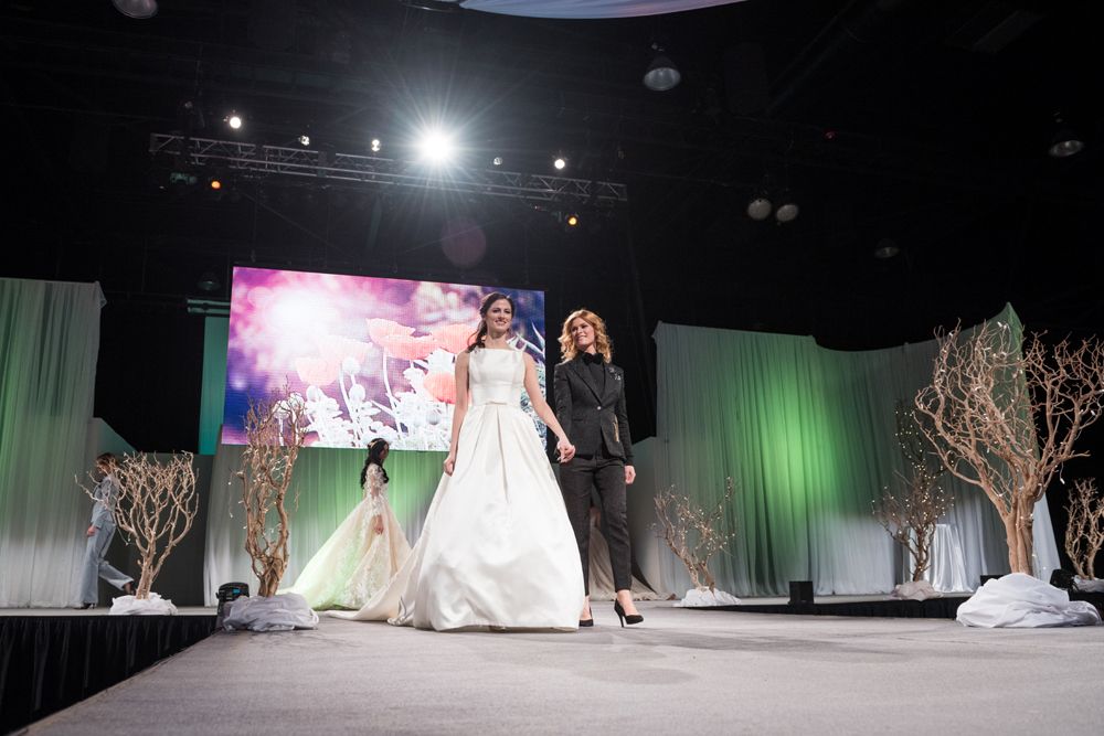 A bride and groom are walking down a runway at a wedding show.