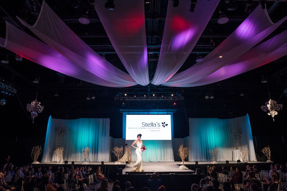 A woman in a wedding dress is walking down a runway at a fashion show.