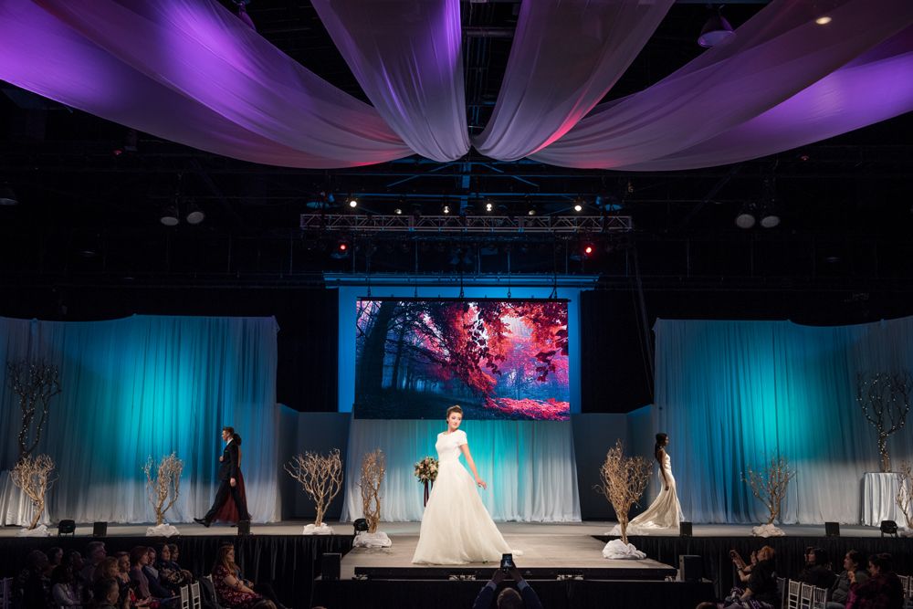 A woman in a wedding dress is walking down a runway at a wedding show.