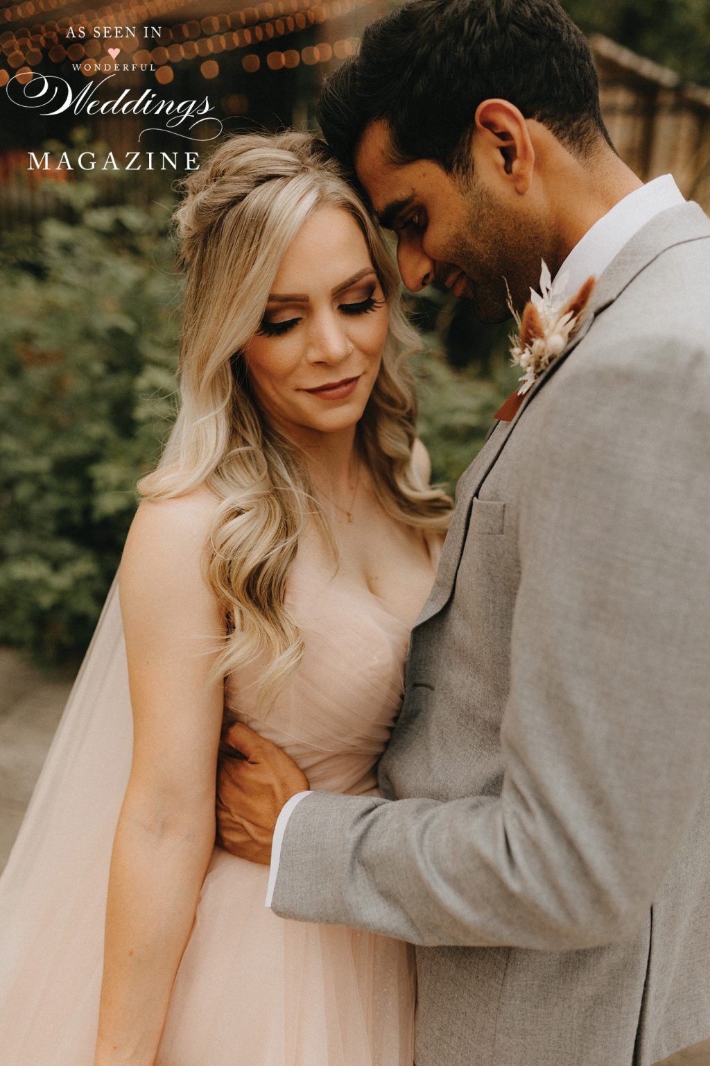 A bride and groom are posing for a picture and the bride is wearing a pink dress.