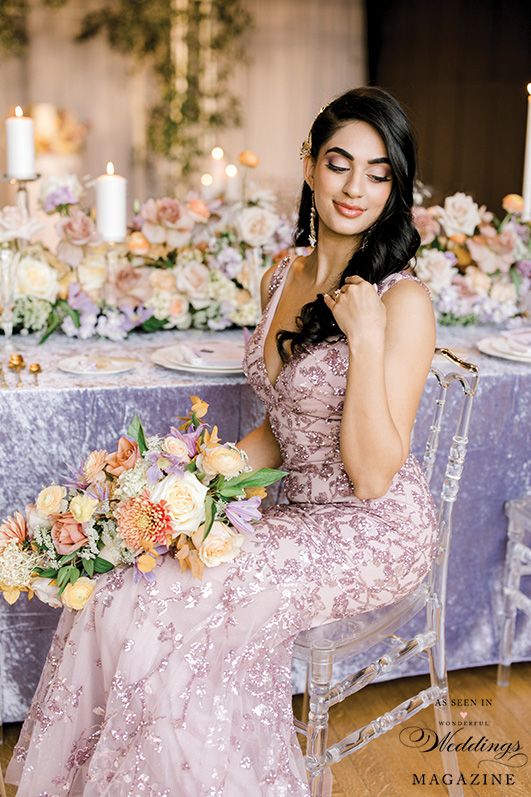 A woman in a pink dress is sitting in a clear chair holding a bouquet of flowers.