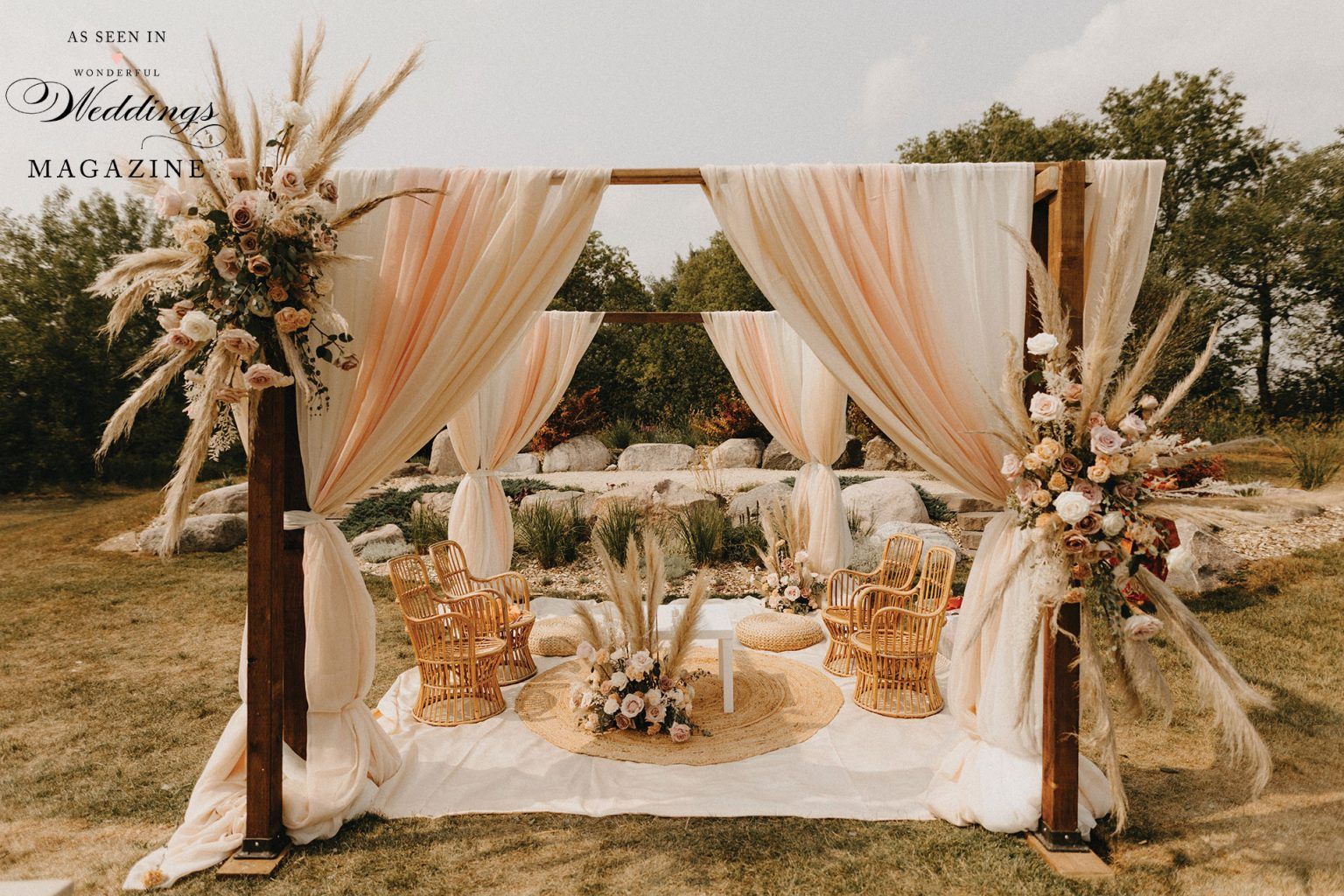 A wooden arch decorated with flowers and curtains is in the middle of a field.