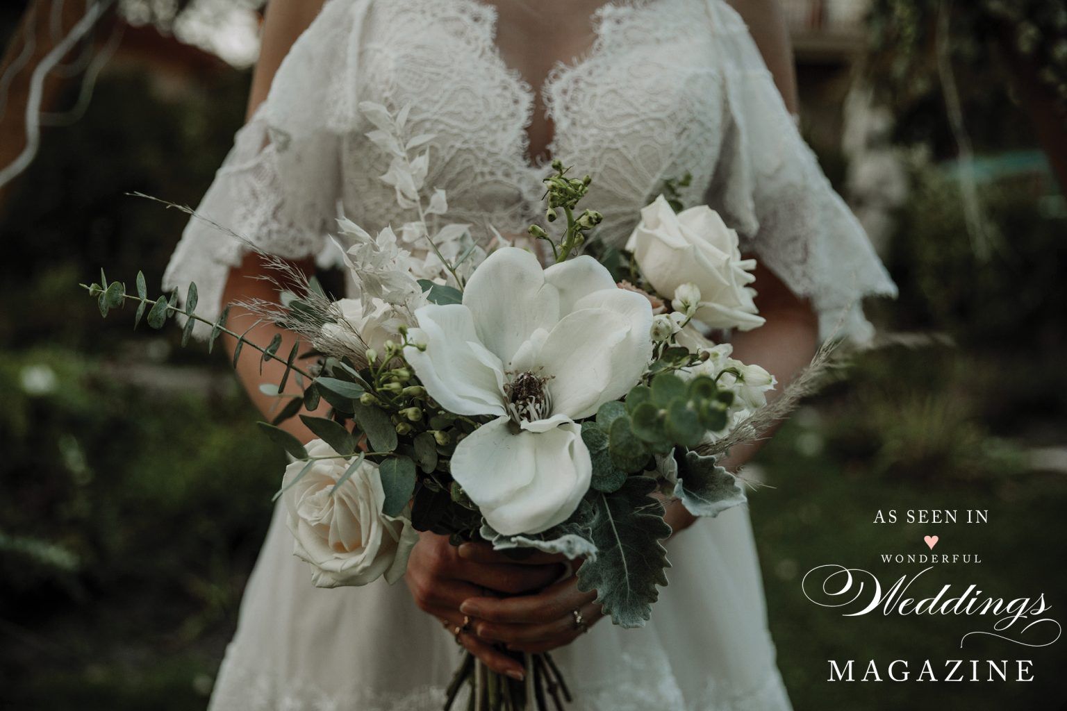 A bride in a white dress is holding a bouquet of white flowers.