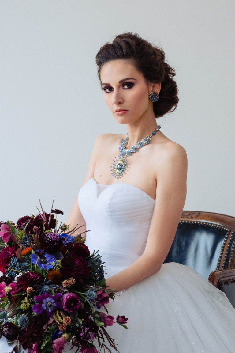 A woman in a white dress is sitting on a chair holding a bouquet of flowers.