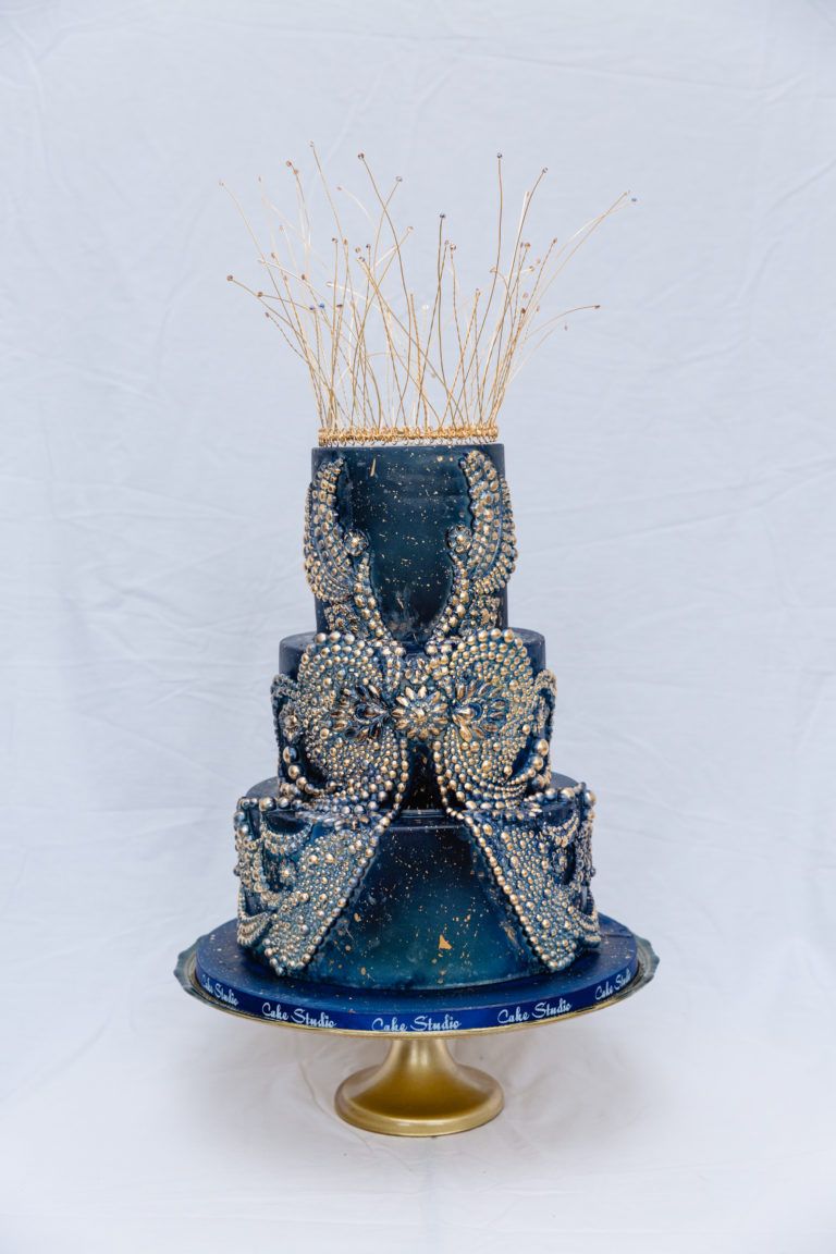 A blue and gold wedding cake with a crown on top of it.