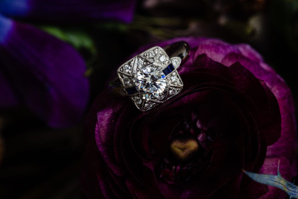 A diamond ring is sitting on top of a purple flower.