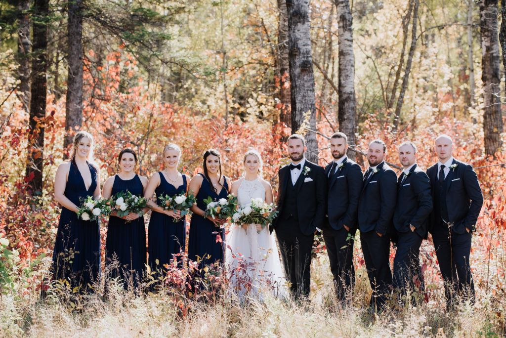 The bride and groom are posing for a picture with their wedding party in the woods.