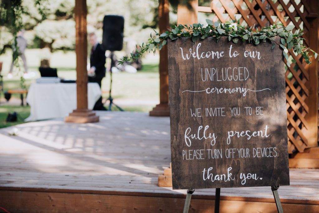 A wooden sign that says `` welcome to our plugged ceremony '' is on a wooden stand.