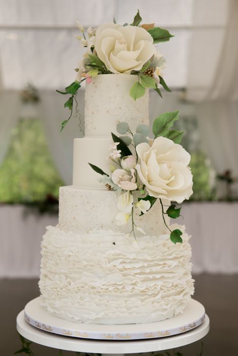 A white wedding cake with ruffles and flowers on top is sitting on a table.