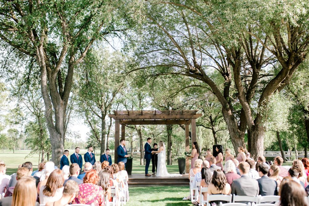 A bride and groom are getting married under a pergola in front of a crowd of people.