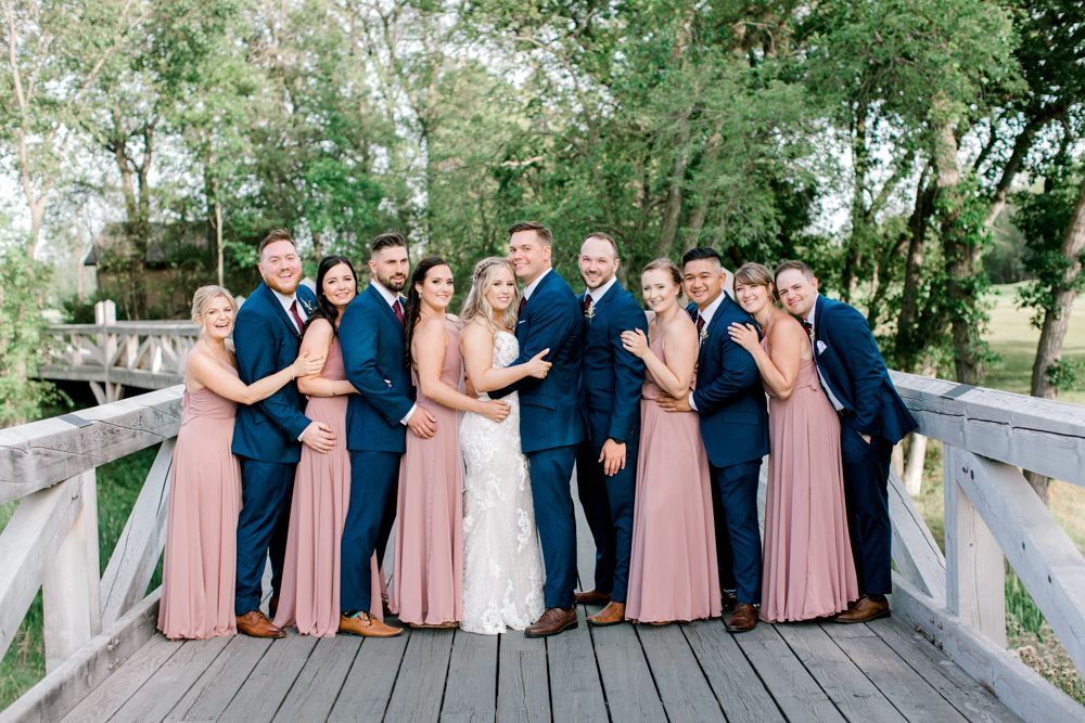The bride and groom are posing for a picture with their wedding party on a bridge.