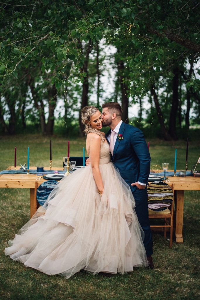 A bride and groom are kissing in front of a table in a field.