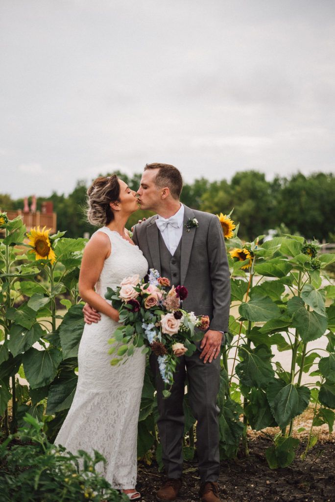 A bride and groom are kissing in a field of sunflowers.