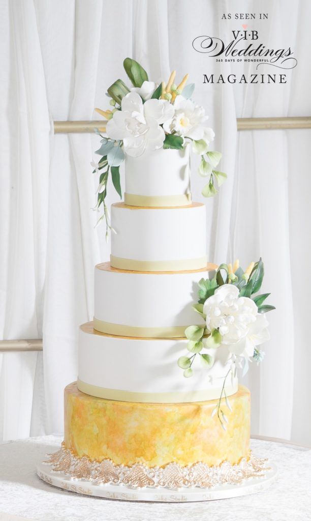A white and gold wedding cake with flowers on top is sitting on a table.