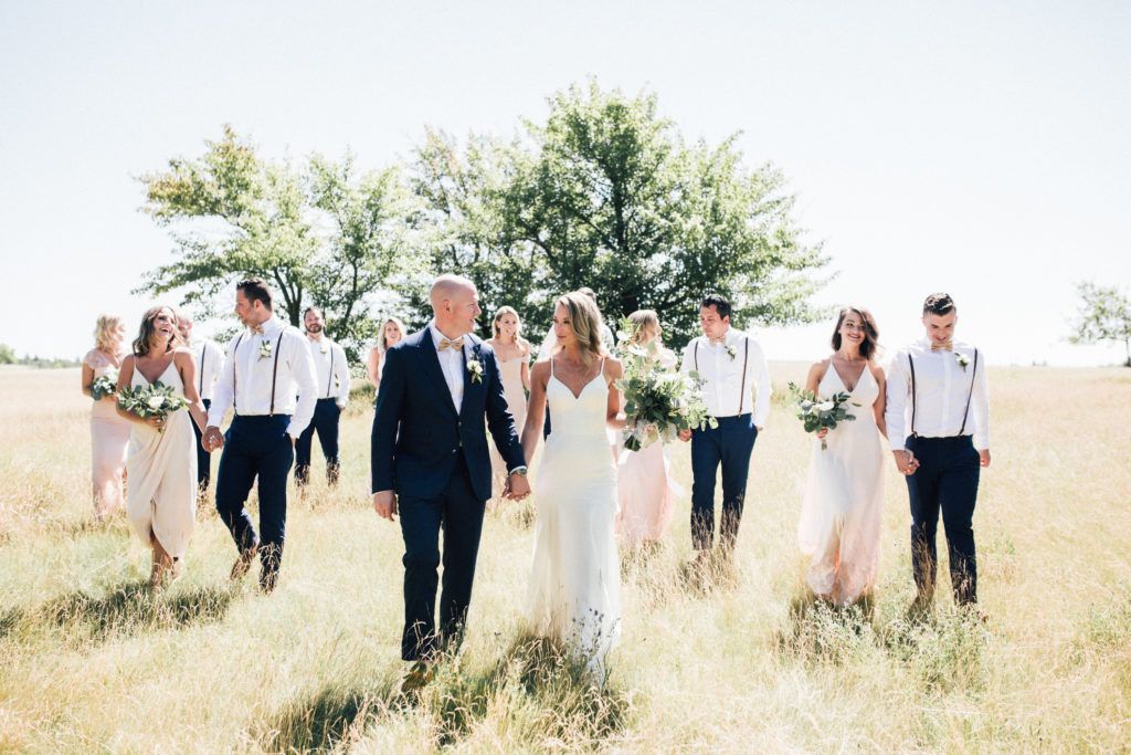 A bride and groom are walking through a field with their wedding party.