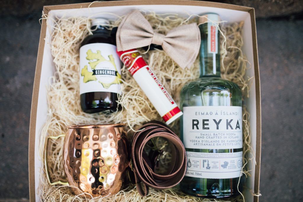 A box filled with bottles , cups , a belt and a bow tie.