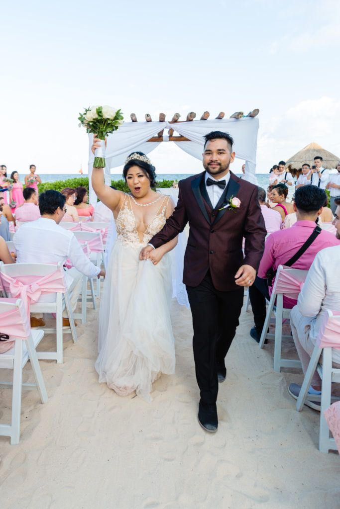 A bride and groom are walking down the aisle at their wedding on the beach.